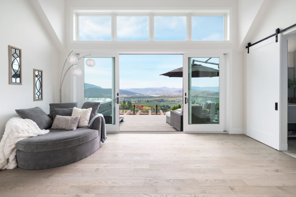 A Beautiful bright custom bedroom with open doors leading to a patio overlooking a view of the Okanagan Valley, a luxury home built by Bercum Builders